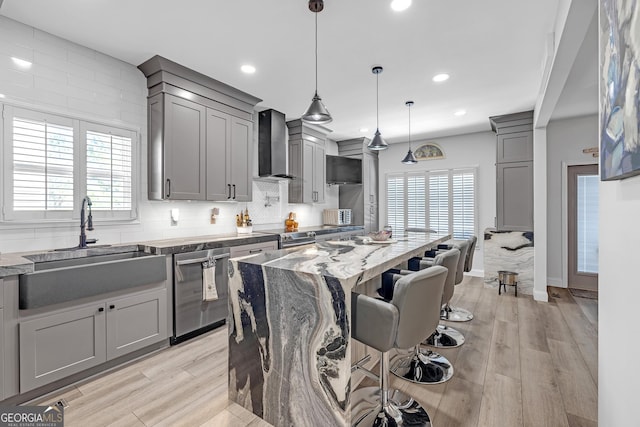 kitchen featuring gray cabinetry, stainless steel appliances, wall chimney range hood, and a sink