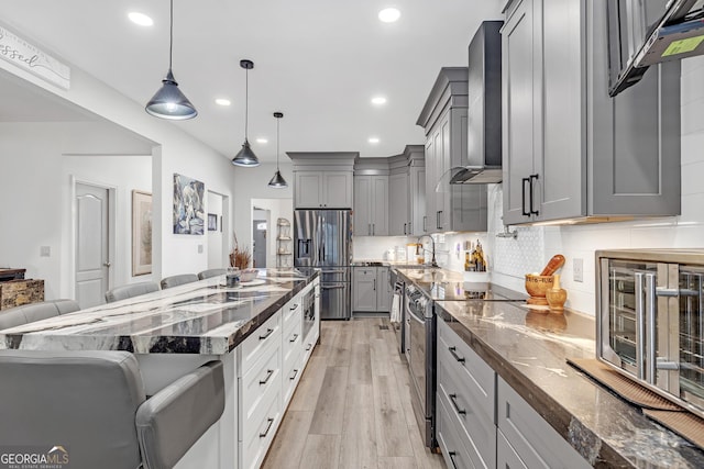 kitchen with dark stone countertops, gray cabinets, decorative backsplash, appliances with stainless steel finishes, and wall chimney range hood