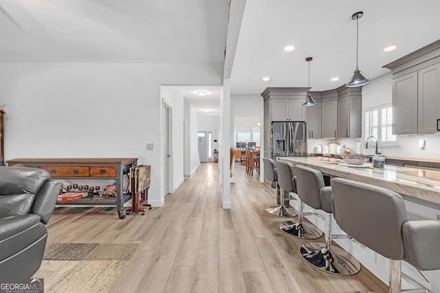 kitchen featuring gray cabinets, light stone counters, open floor plan, light wood-style floors, and a breakfast bar area