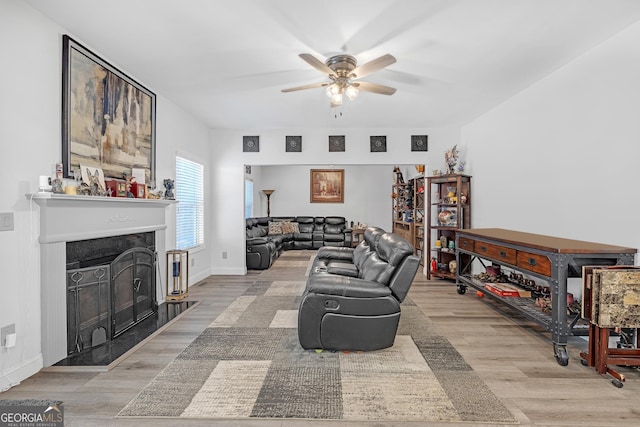 living room featuring a premium fireplace, wood finished floors, baseboards, and ceiling fan