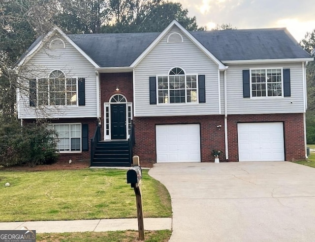 bi-level home featuring driveway, brick siding, an attached garage, and a front yard