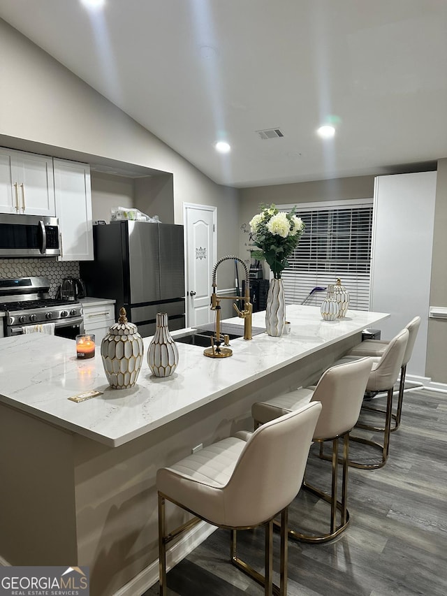 kitchen with white cabinetry, lofted ceiling, a breakfast bar area, and appliances with stainless steel finishes