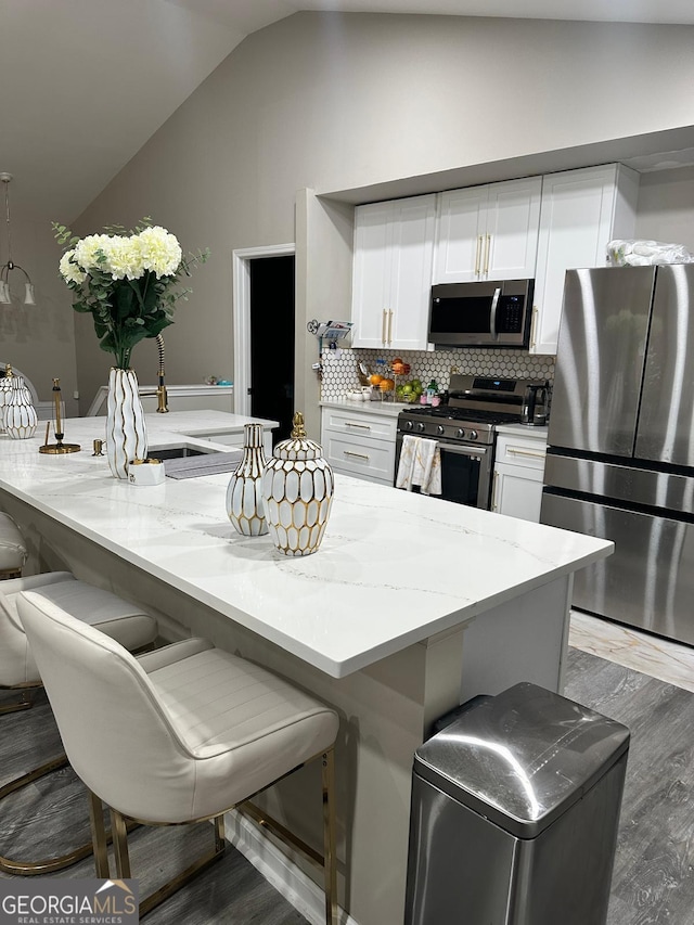 kitchen featuring tasteful backsplash, lofted ceiling, light stone counters, stainless steel appliances, and white cabinetry