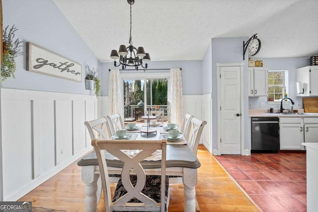 dining space featuring light wood finished floors, wainscoting, a textured ceiling, a decorative wall, and a chandelier