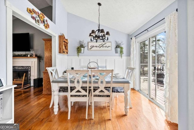 dining room with a textured ceiling, wood finished floors, a fireplace, wainscoting, and vaulted ceiling