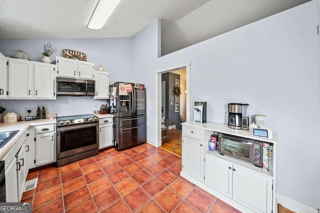 kitchen with lofted ceiling, stainless steel appliances, light countertops, white cabinets, and tile patterned floors