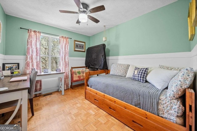 bedroom with visible vents, a ceiling fan, wainscoting, and a textured ceiling