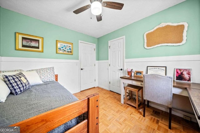 bedroom featuring wainscoting, a textured ceiling, and ceiling fan