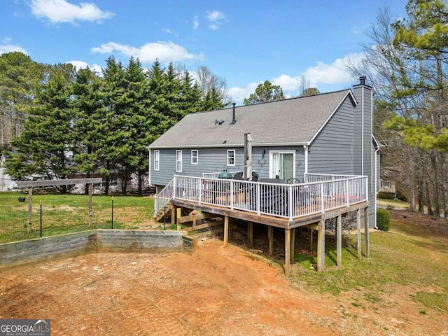 rear view of house with a chimney, a lawn, a wooden deck, and roof with shingles