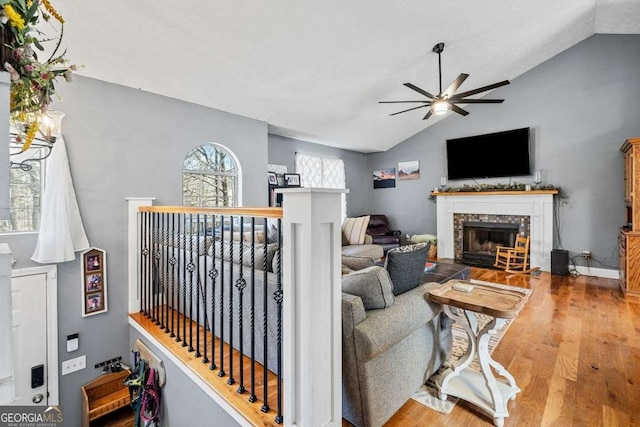 living room with a ceiling fan, wood finished floors, a fireplace, and vaulted ceiling