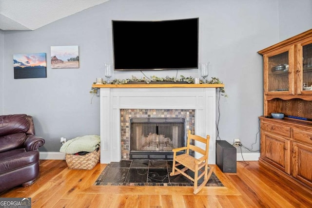 living area featuring a tiled fireplace, lofted ceiling, baseboards, and wood finished floors