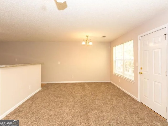 carpeted empty room with a textured ceiling, visible vents, baseboards, and a chandelier