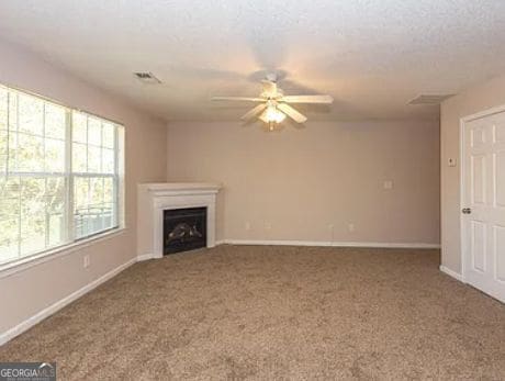 unfurnished living room featuring baseboards, carpet floors, a ceiling fan, and a fireplace