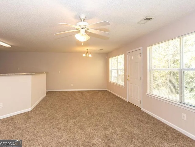 carpeted spare room featuring visible vents, baseboards, a textured ceiling, and ceiling fan with notable chandelier