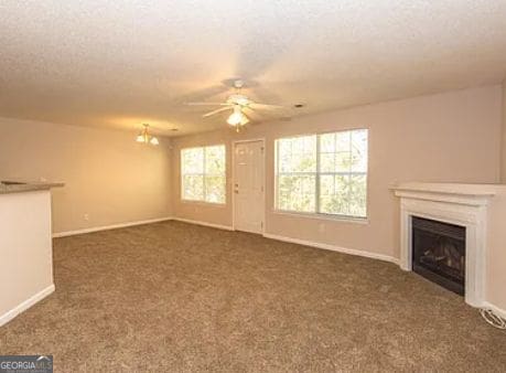 unfurnished living room with a textured ceiling, dark carpet, a fireplace, baseboards, and ceiling fan