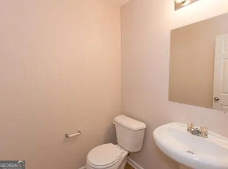 half bathroom with toilet, baseboards, and a sink