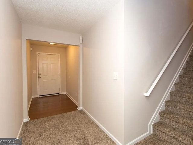 corridor featuring stairway, baseboards, a textured ceiling, and carpet