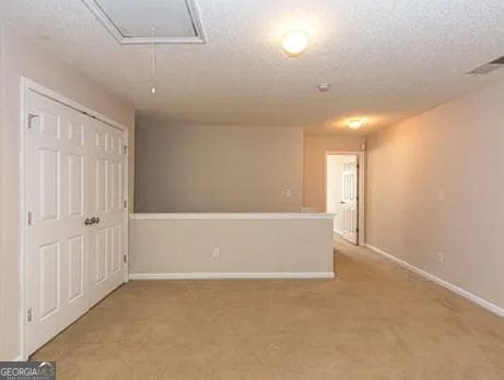 spare room with visible vents, a textured ceiling, baseboards, light colored carpet, and attic access