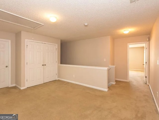 interior space with a closet, light colored carpet, attic access, and baseboards