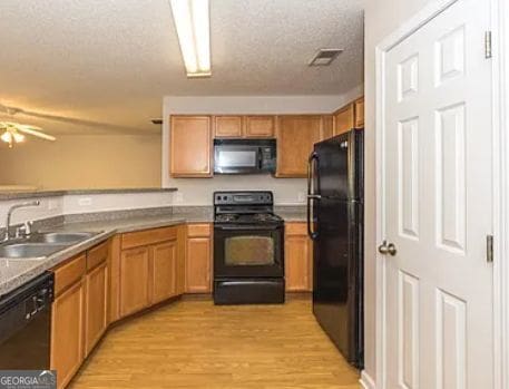 kitchen featuring visible vents, black appliances, a sink, a textured ceiling, and light wood finished floors