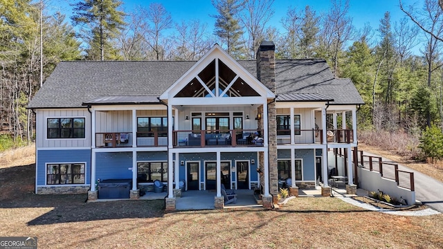 back of property with a patio, a balcony, board and batten siding, and a chimney