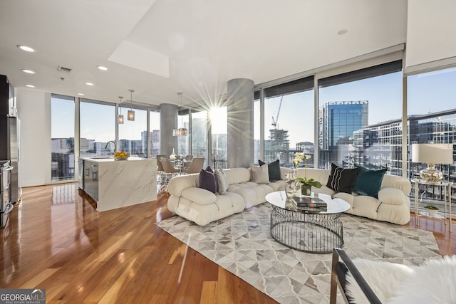 living area with visible vents, a healthy amount of sunlight, floor to ceiling windows, light wood-type flooring, and a view of city