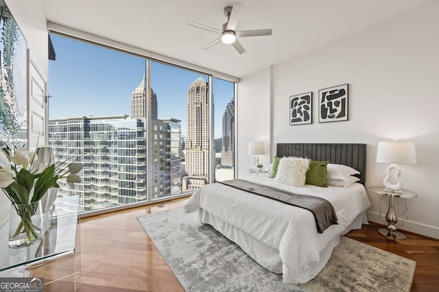 bedroom featuring a ceiling fan, wood finished floors, baseboards, expansive windows, and a city view