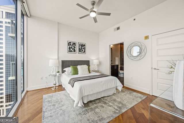 bedroom with wood finished floors, visible vents, baseboards, floor to ceiling windows, and ensuite bathroom