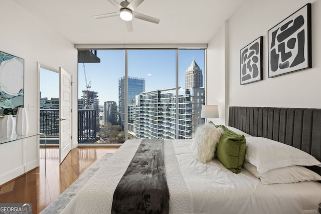 bedroom featuring a city view, access to outside, expansive windows, wood finished floors, and ceiling fan