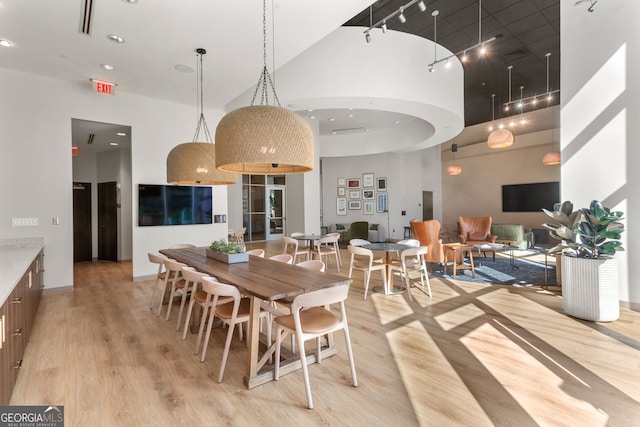 dining room featuring light wood-style flooring, rail lighting, baseboards, and a towering ceiling