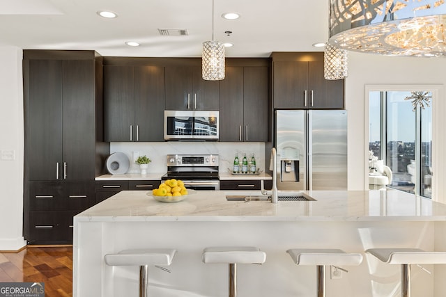 kitchen featuring a sink, appliances with stainless steel finishes, a breakfast bar area, and dark wood finished floors