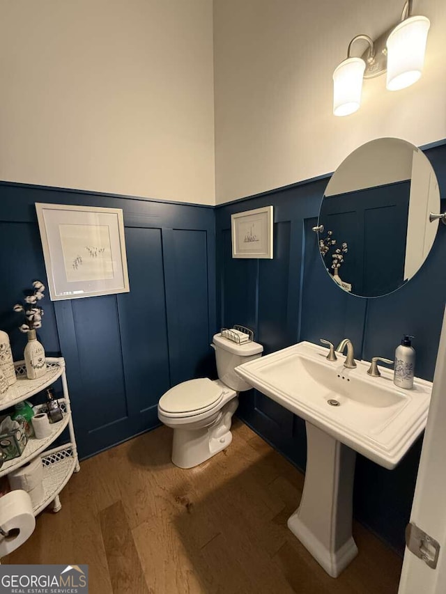 half bath with a decorative wall, toilet, wood finished floors, and a wainscoted wall