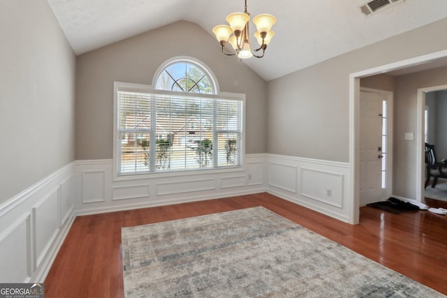 unfurnished dining area featuring wood finished floors, visible vents, an inviting chandelier, lofted ceiling, and wainscoting