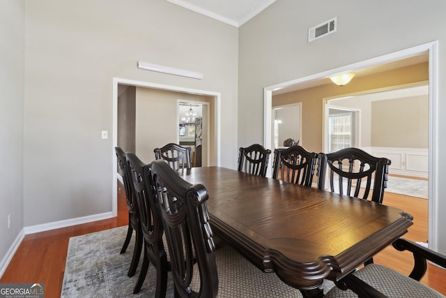 dining room with visible vents, a notable chandelier, wood finished floors, a high ceiling, and crown molding