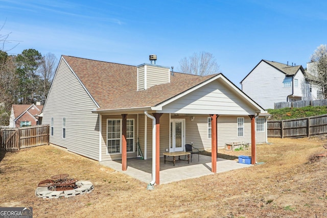 rear view of house featuring a shingled roof, a fire pit, a fenced backyard, and a patio area