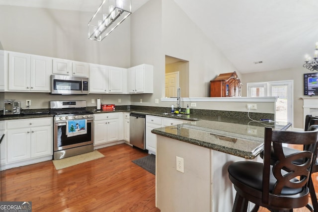 kitchen with a sink, stainless steel appliances, a peninsula, a breakfast bar area, and white cabinets