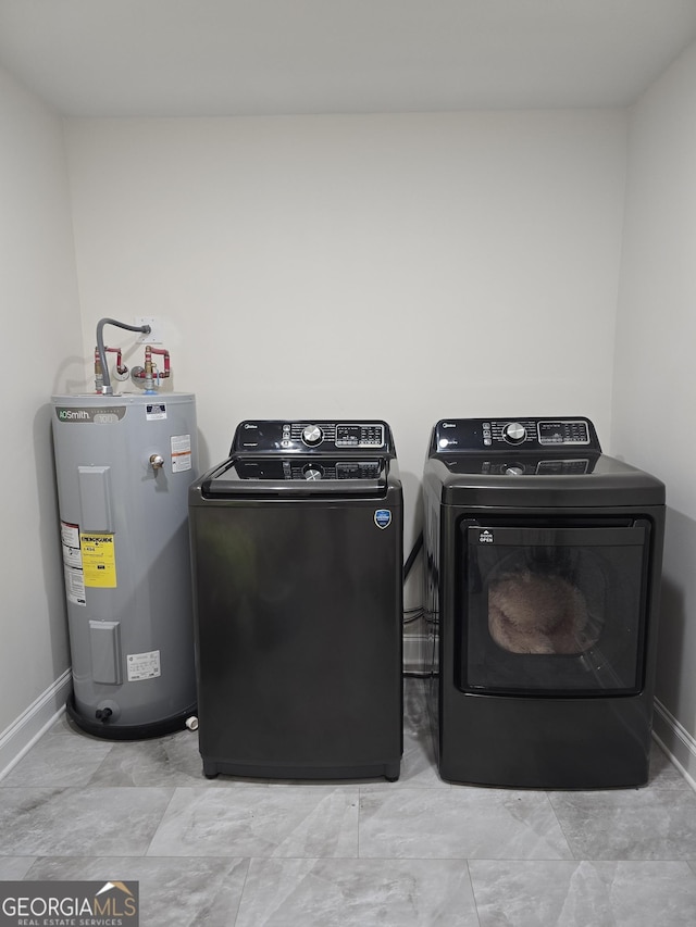 clothes washing area featuring laundry area, washing machine and dryer, water heater, and baseboards