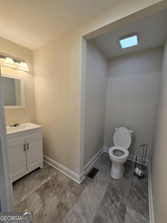 half bath with visible vents, baseboards, toilet, and vanity