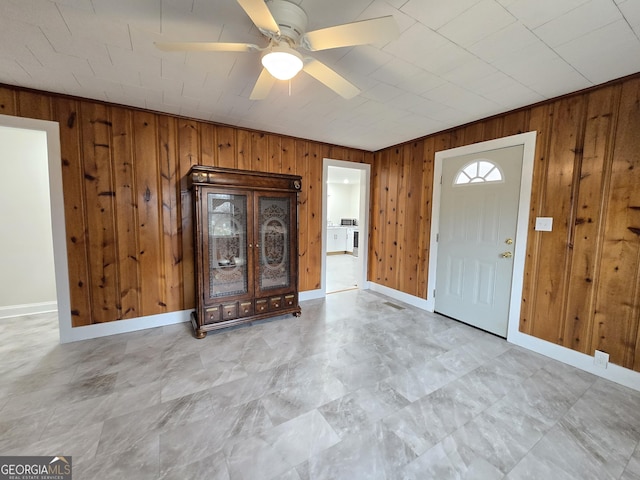 foyer with ceiling fan, baseboards, and wood walls