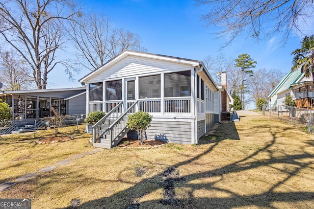 view of front of house featuring fence, stairs, a front yard, a chimney, and a sunroom