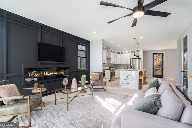 living room with a glass covered fireplace, recessed lighting, a decorative wall, and light wood-style floors