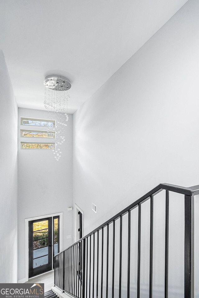 staircase featuring a high ceiling, a healthy amount of sunlight, visible vents, and a chandelier