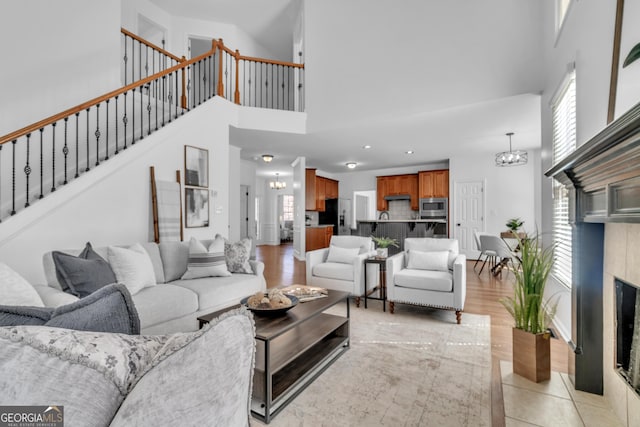 living room featuring stairs, a tiled fireplace, a high ceiling, and a chandelier