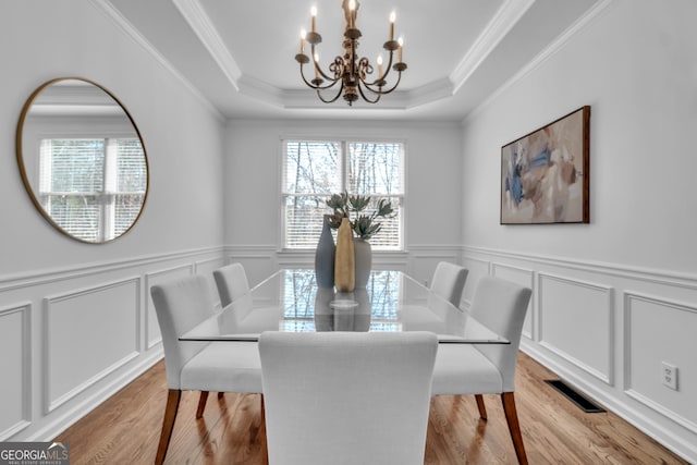 dining room with visible vents, a tray ceiling, a decorative wall, a notable chandelier, and light wood-type flooring