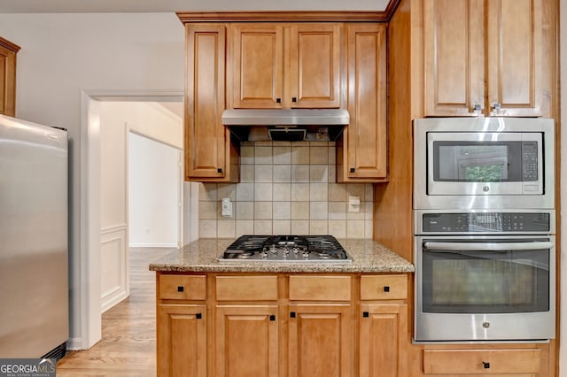 1654 Summersweet Ln, Dacula, GA 30019 - kitchen with stainless steel appliances, under cabinet range hood, decorative backsplash, light stone countertops, and light wood finished floors