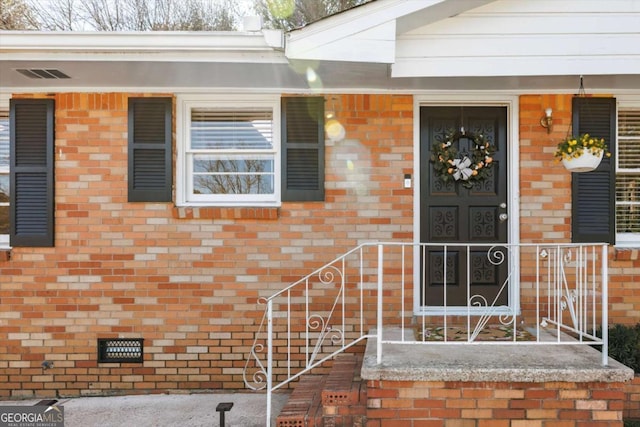 entrance to property with visible vents, brick siding, and crawl space