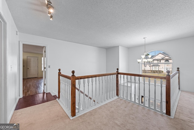 hallway with an upstairs landing, a textured ceiling, wood finished floors, carpet, and a chandelier