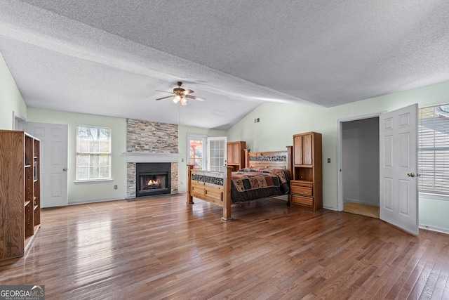 bedroom featuring a textured ceiling, vaulted ceiling, wood finished floors, and a large fireplace