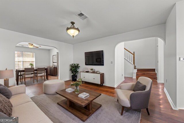 living area with arched walkways, stairs, baseboards, and wood finished floors