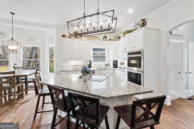 kitchen featuring stainless steel double oven, arched walkways, light wood-style floors, crown molding, and decorative backsplash